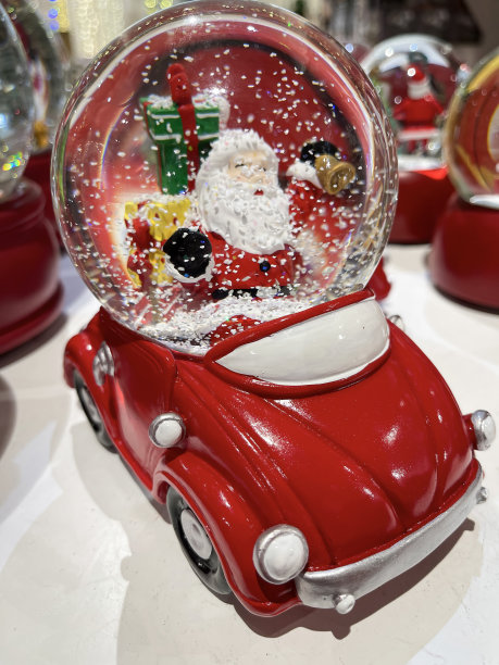 一辆红色的车，上面挂着一个雪花圣诞球，圣诞老人在里面带着圣诞礼物，里面飘着雪花图片下载
