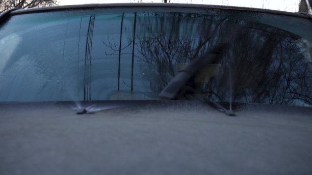 汽车刮水器清洁汽车玻璃，并将水溅到挡风玻璃上。一个人坐在汽车里，控制着一个机械装置。图片下载