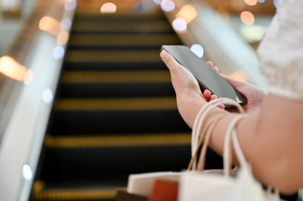 特写，年轻的亚洲女性使用她的智能手机，拿着她的购物袋图片下载