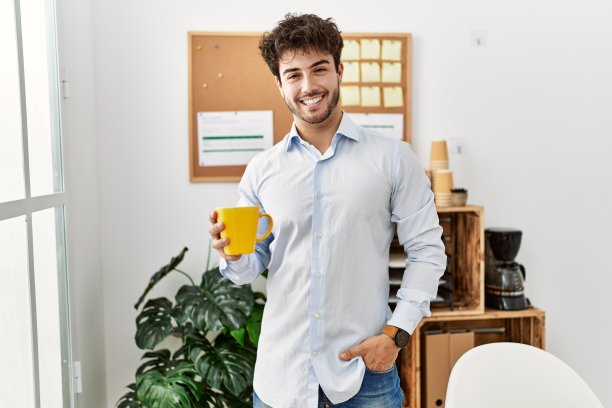 年轻的西班牙商人微笑快乐地在办公室喝咖啡。图片下载
