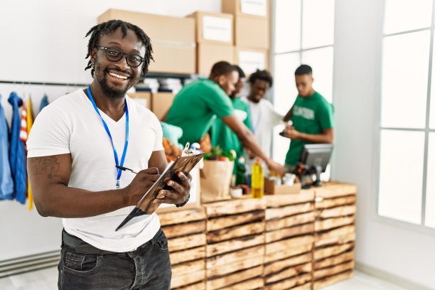 一群年轻的非裔美国志愿者在慈善中心工作。男人微笑着快乐地在写字板上写字。图片下载