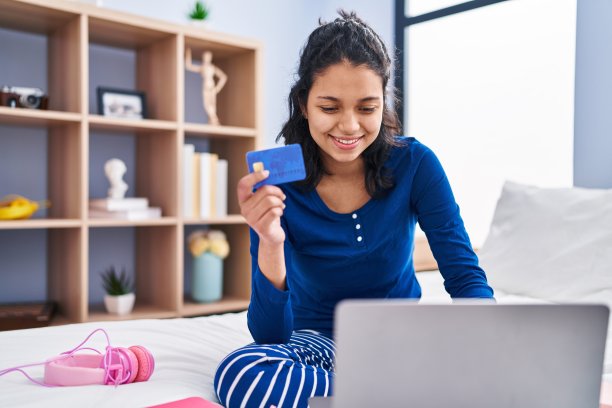 年轻的拉丁女子用笔记本电脑和信用卡坐在卧室的床上图片下载