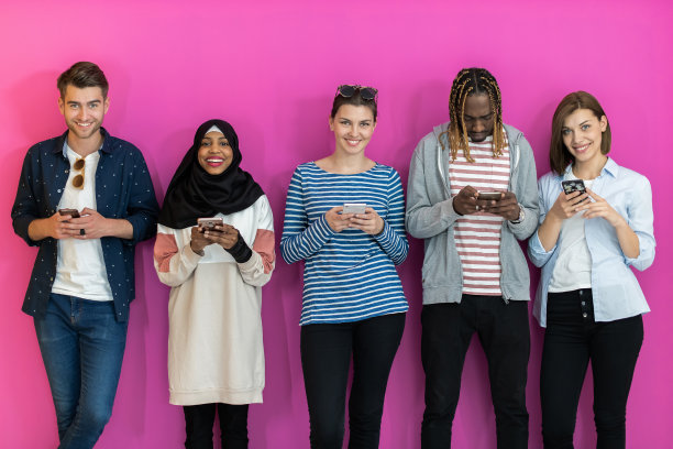 各种各样的青少年在彩色背景前使用移动设备在摄影棚里摆姿势拍照图片下载