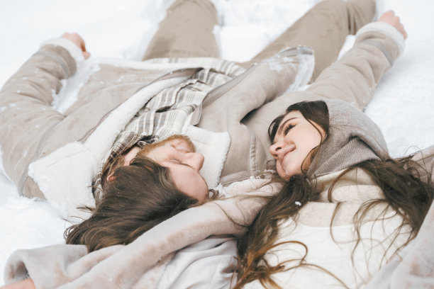 浪漫的雪花爱情故事。年轻的情侣男孩女孩躺着，在下雪的冬天森林里玩树。穿着时髦保暖的衣服，皮大衣，羊毛夹克，披肩，散步，玩乐，大笑。约会,周末假期图片下载