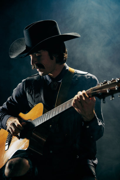 肖像男子留着小胡子，穿着乡村风格的衣服，弹奏吉他，在深蓝色背景与烟雾隔离。浪漫图片下载