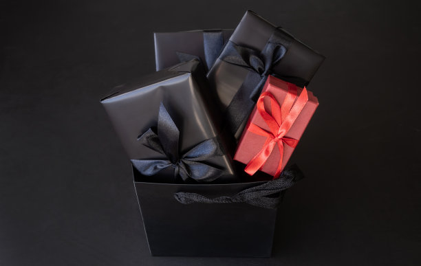 礼品盒包装在黑色的纸与黑色的蝴蝶结在一个包装在黑暗的背景。节日的概念。放置文字或广告的地方。圣诞节。“黑色星期五”。图片下载