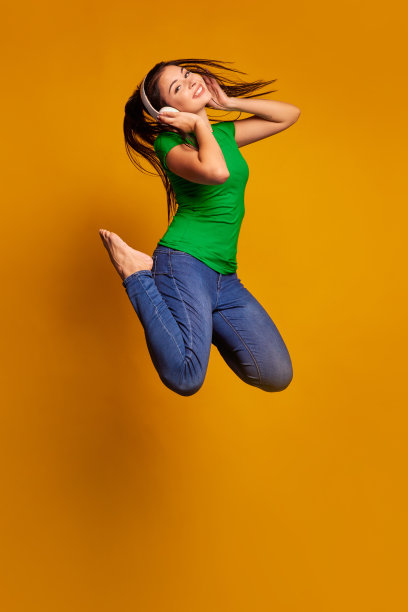跳得很高，飞得很高。年轻女子的肖像在彩色工作室背景。漂亮的女模特戴着耳机。人类情感的概念，面部表情，青春，销售，广告。图片下载