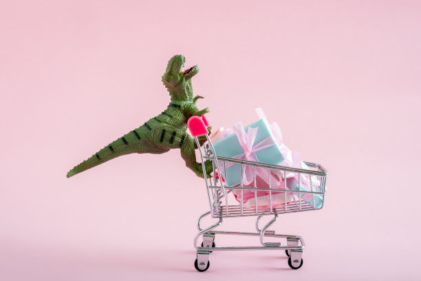 有趣的绿色恐龙玩具购物车装满了礼物盒在一个柔软的粉色背景。图片下载
