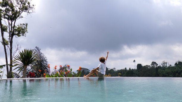 白人妇女坐在泳池边享受她的天堂之旅。一个美丽的女人在天空和水之间的假期在一个美丽的天堂在热带。图片下载