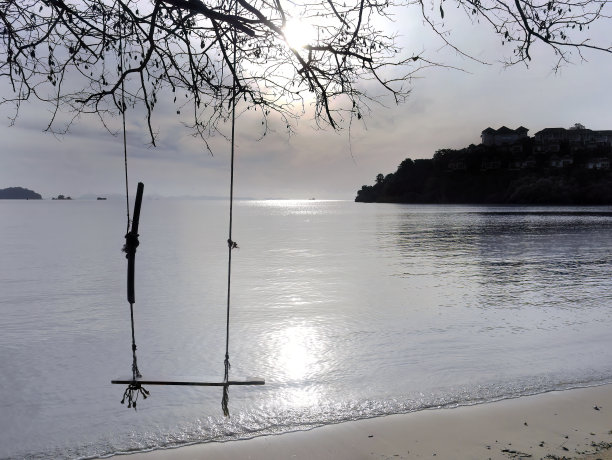 日出，清晨的木秋千挂在沙滩上的树下，以大海为背景。泰国普吉岛图片下载