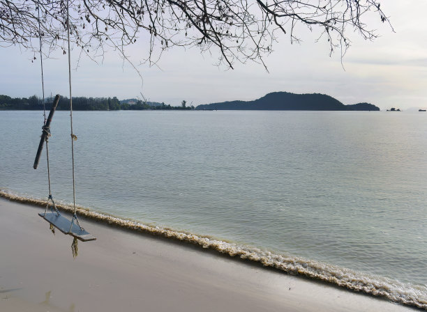 木制秋千悬挂在沙滩上的树下，以大海为背景。泰国普吉岛。图片下载
