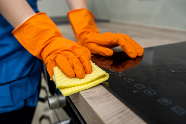 戴着橙色连指手套的漂亮女性双手擦拭着厨房表面图片下载