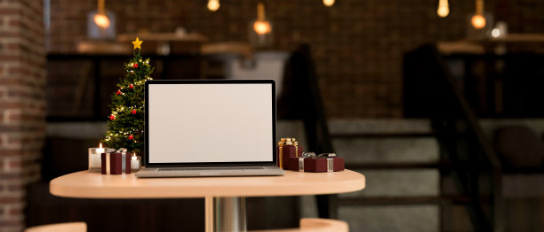 工作区桌面与笔记本电脑，圣诞树，礼物和蜡烛模糊的背景图片下载