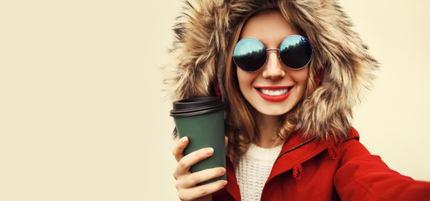 画像快乐微笑的妇女伸出手与智能手机自拍穿着夹克与皮草帽图片下载