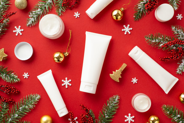 冬季护肤化妆品概念。顶视图照片管奶油罐冷杉树枝在霜槲寄生浆果金色的小饰物装饰夹子和雪花孤立的红色背景与空白图片下载