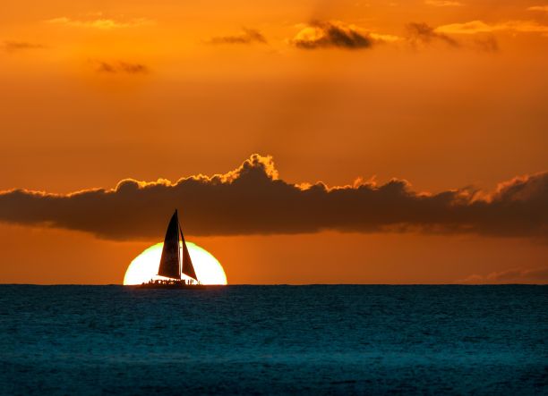 在金色的天空下，一艘帆船的剪影在金色的日落天空下的海洋图片下载