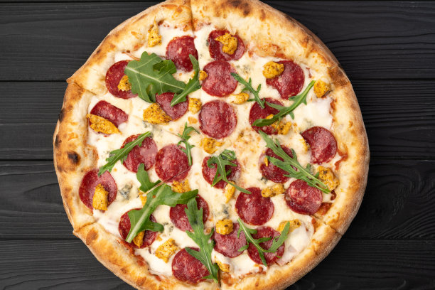 自制新鲜披萨与意大利腊肠，圣女果和芝麻菜在黑色木制。副本的空间。俯视图食物照片。平的。意大利美食图片下载