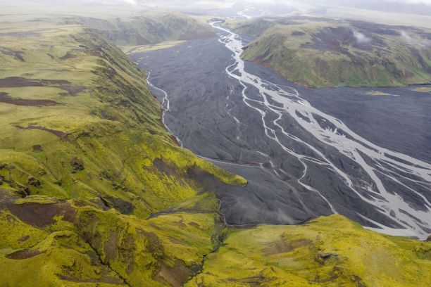 在冰岛卡特拉地质公园，一条河流从绿色覆盖的山上流过的航拍照片图片下载