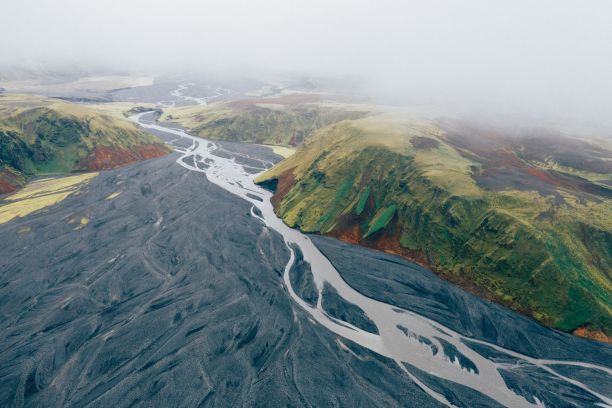 在冰岛卡特拉地质公园，一条河流从绿色覆盖的山上流过的航拍照片图片下载