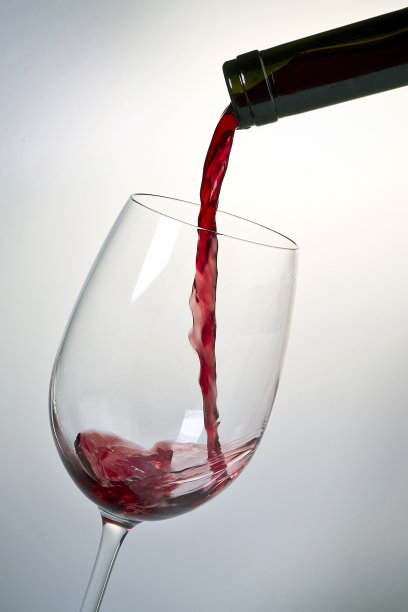 在白色背景下，红酒从瓶子里倒进玻璃杯的垂直镜头图片下载