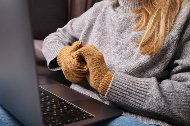 一个年轻的女人坐在寒冷的房间里，披着毯子，戴着手套。在笔记本电脑上工作。天冷的时候还能顶着压力工作图片下载