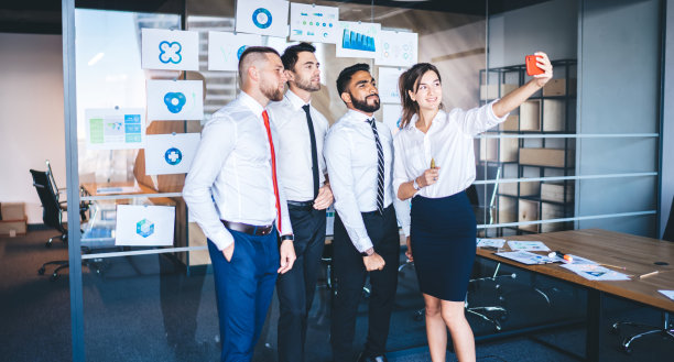 不同的男性和女性同事享受在现代办公室内一起自拍的时间，成功的伴侣在室内通过应用程序点击移动图像图片下载