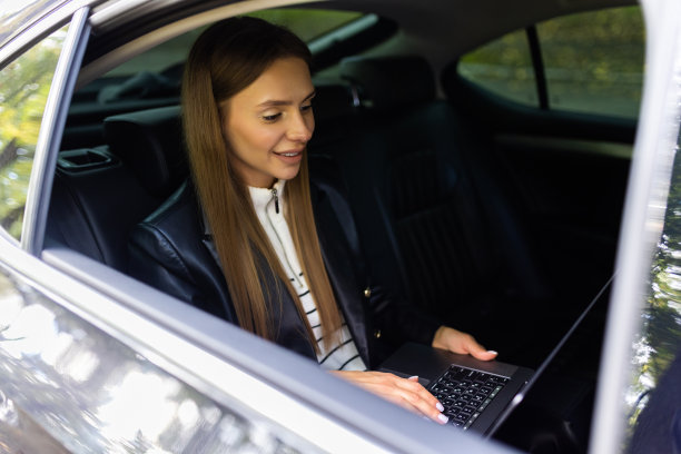 美丽的商业女性正在使用笔记本电脑，微笑着坐在汽车后座上图片下载