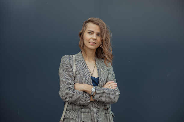 自信，体贴，微笑金发女商人凌乱的发型在灰色夹克交叉手臂在蓝色的看法图片下载