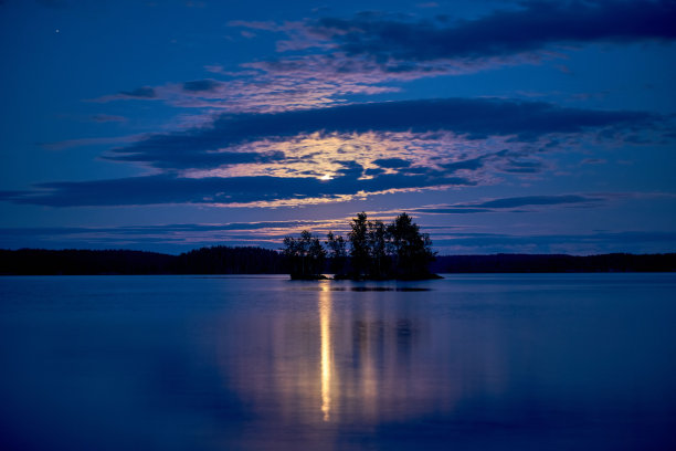 湖水反射着月光，背景是树木和多云的夜空图片下载