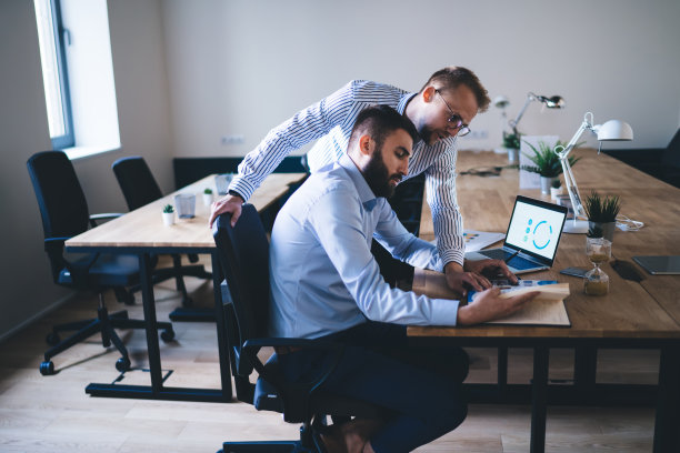 认真的年轻男性企业家一起进行研究，使用技术和讨论想法，聪明的白人男性同事在办公室开会时阅读财务报告，彼此交谈图片下载