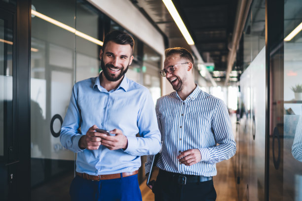 愉快的男同事在友好的工作环境中享受伙伴关系，走在办公室走廊上，笑着讨论智能手机上的网络出版物，快乐的员工满意图片下载