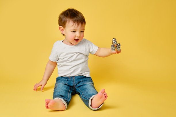 蹒跚学步的婴儿在一根棍子上玩音乐拨浪鼓，工作室黄色背景。快乐的儿童音乐家演奏打击乐乐器，复制空间。一岁零四个月的孩子图片下载