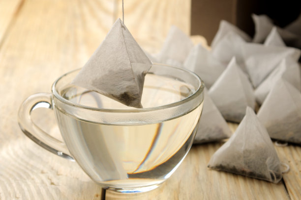 将一杯沸水和一个茶包金字塔放入杯中。特写镜头。图片下载