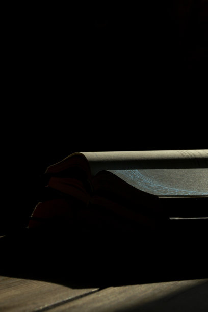 抽象照片——一本打开的书躺在黑暗中。黑漆漆的房间里翻开的书里写着奇怪的符号。在黑暗中，一束光落在一本打开的书上。图片下载