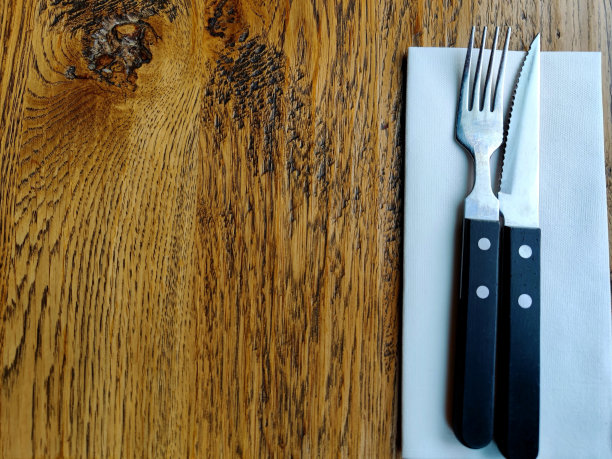 餐厅的木桌上放着没有标记的刀叉餐具和一张空白的白色餐巾纸图片下载