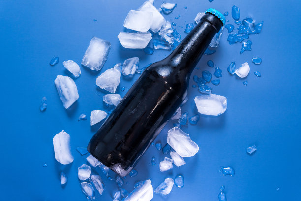 顶视图的玻璃啤酒瓶上的蓝色表面与冰图片下载