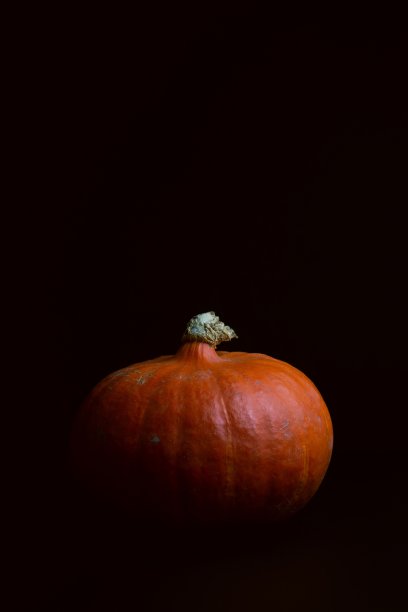 在黑色背景上垂直拍摄一个美味的橙色南瓜图片下载