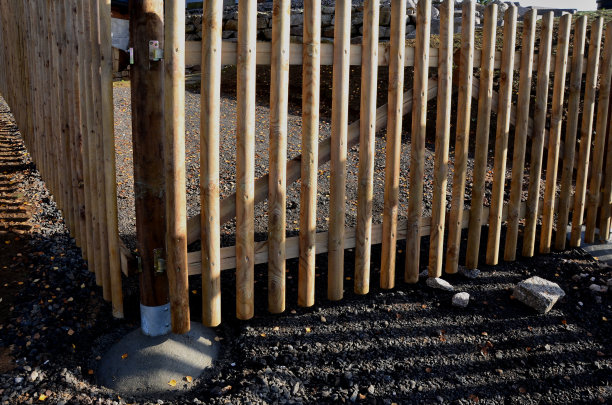 天然木板制成的木栅栏。这些柱子是用粗糙的灰色花岗岩制成的。在山上用栅栏围地。草地树木阳光。木板在切尖处图片下载