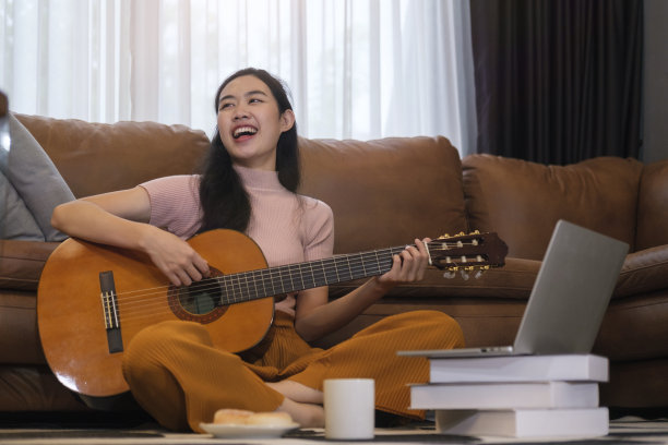快乐的年轻女子坐在舒适的客厅和弹吉他。图片下载
