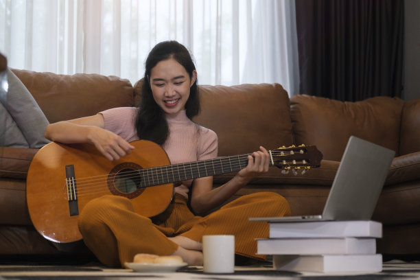 快乐的年轻女子在客厅玩吉他，在家里度过闲暇时光。图片下载