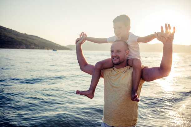 年轻人和他的男孩在海滩度假时一起玩，一起花时间。幸福的父亲拥抱着儿子。图片下载