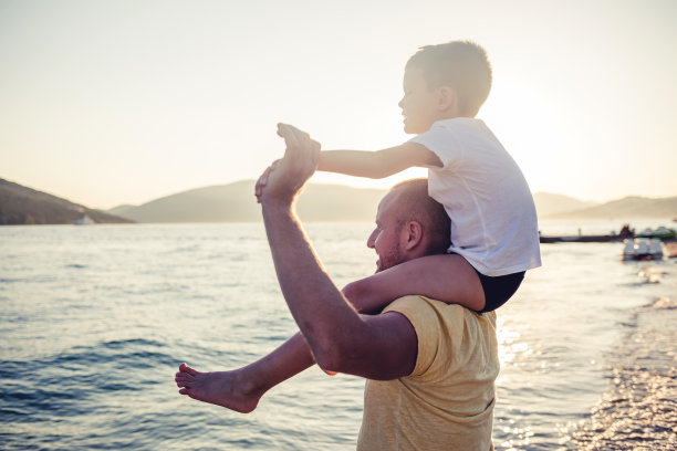 年轻人和他的男孩在海滩度假时一起玩，一起花时间。幸福的父亲拥抱着儿子。图片下载