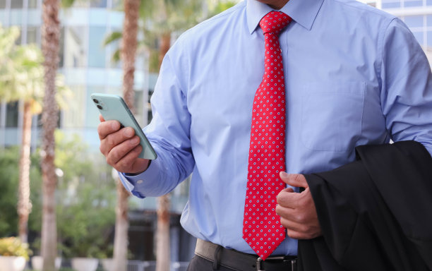 商人穿着夹克，打着红色领带，手里拿着手机站在街上图片下载
