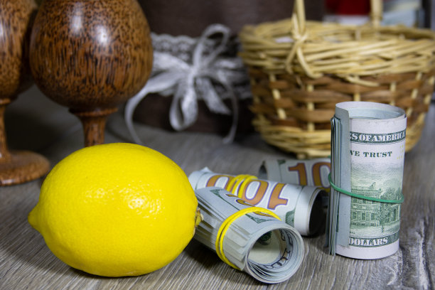一张灰色的木桌上，卷起来的美元钞票和黄色的柠檬的特写图片下载
