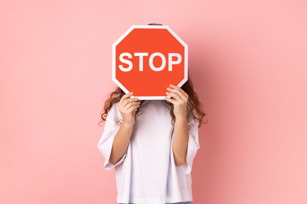匿名小女孩用停止标志遮住脸，举着红色交通标志，禁止进入。图片下载