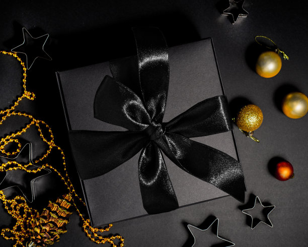 礼物在一个黑色的包装与黑色蝴蝶结背景金色圣诞装饰在黑色的背景图片下载