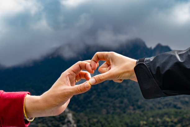 两只手相互接触，形成了心形的形状，背景是多山和多云，只有手被照亮图片下载