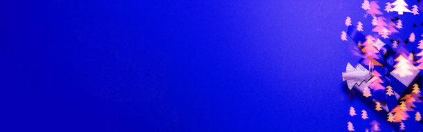 旗帜的棕色纸礼盒与蓝色缎带蝴蝶结蓝色背景与金色散焦和木制圣诞树形状与闪光。平铺圣诞父亲母亲节和礼物的概念图片下载