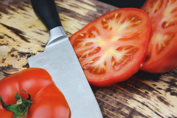 刀放在可切的西红柿旁边。新鲜成熟的番茄放在木板上。图片下载