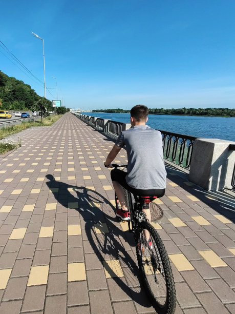 透视图中，一个十几岁的男孩骑着自行车在铺着瓷砖的人行道上。后视图片下载